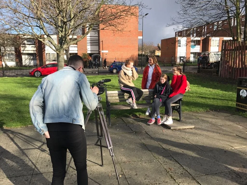 Theatre Group filming outdoors in a park with a man behind a tripod